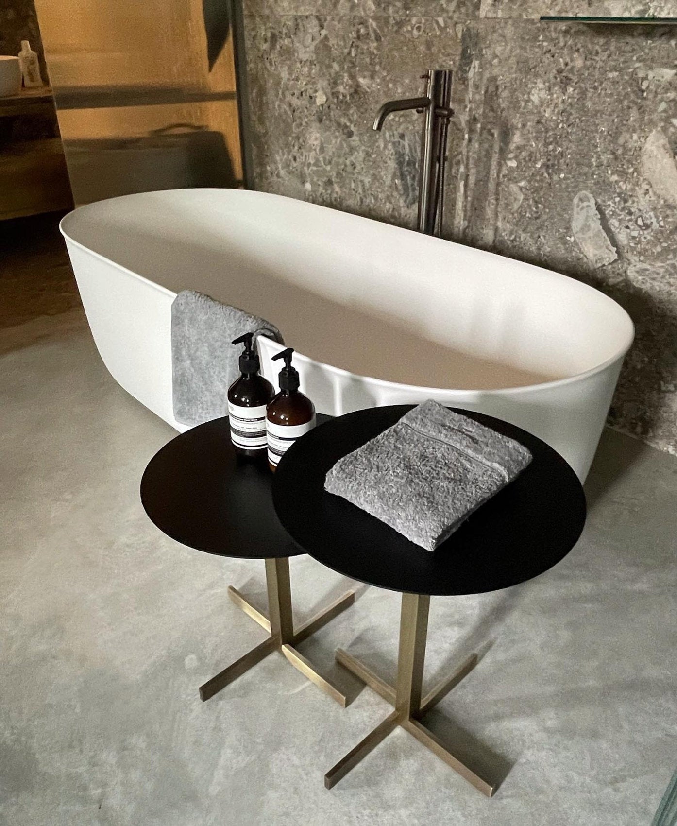 Tavolini Xo Brass di xam con base in ottone satinato e top nero in ferro accanto a vasca freestanding