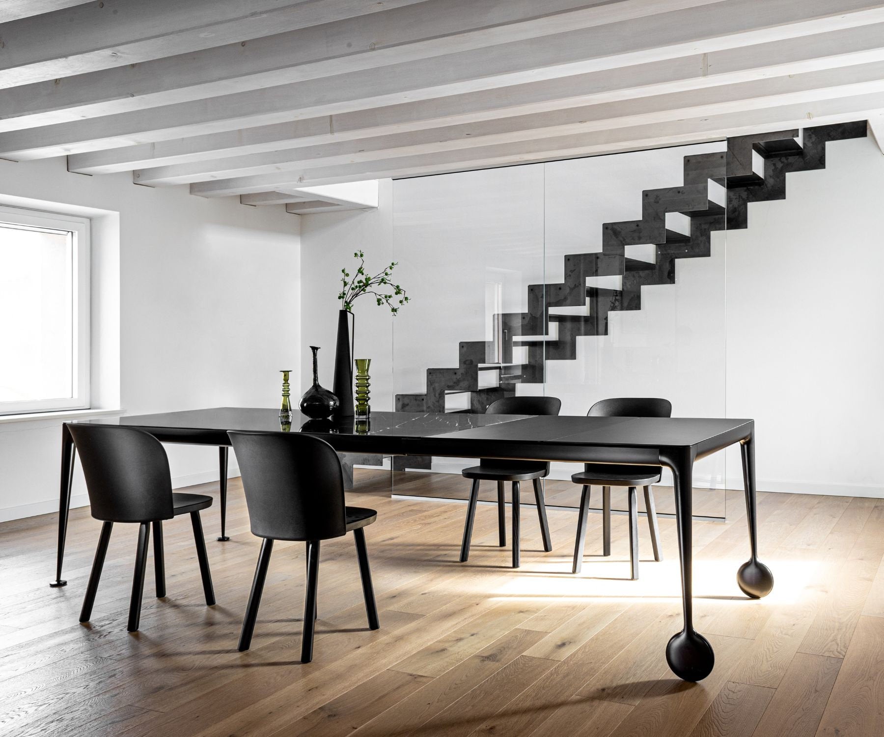 Tavolo nero con gambe scultoree e sedie nere in legno in soggiorno contemporaneo con scala geometrica