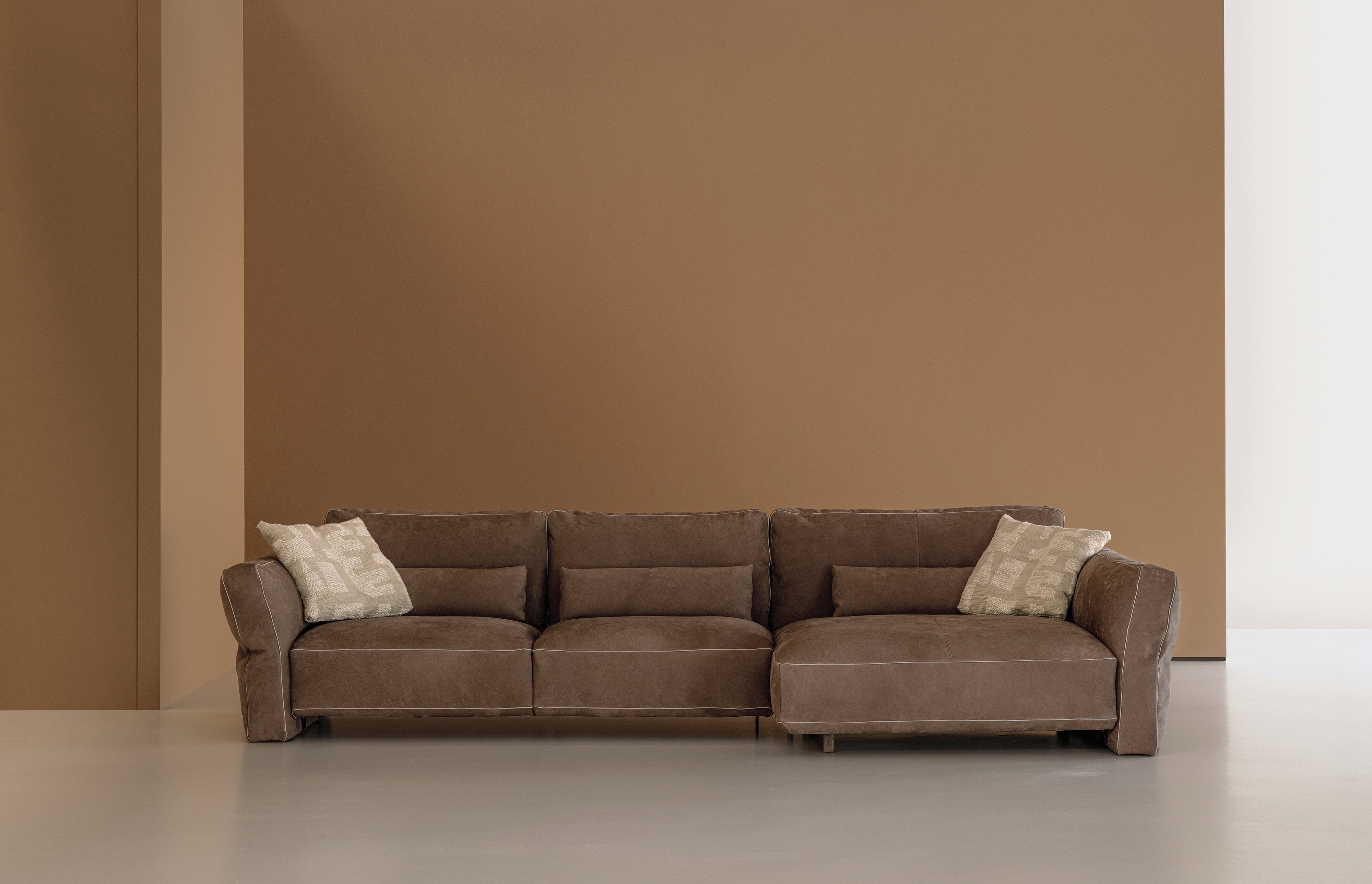 Divano modulare Loden di Cierre1972 in pelle marrone, composizione angolare con cuscini decorativi chiari su sfondo monocromatico beige
