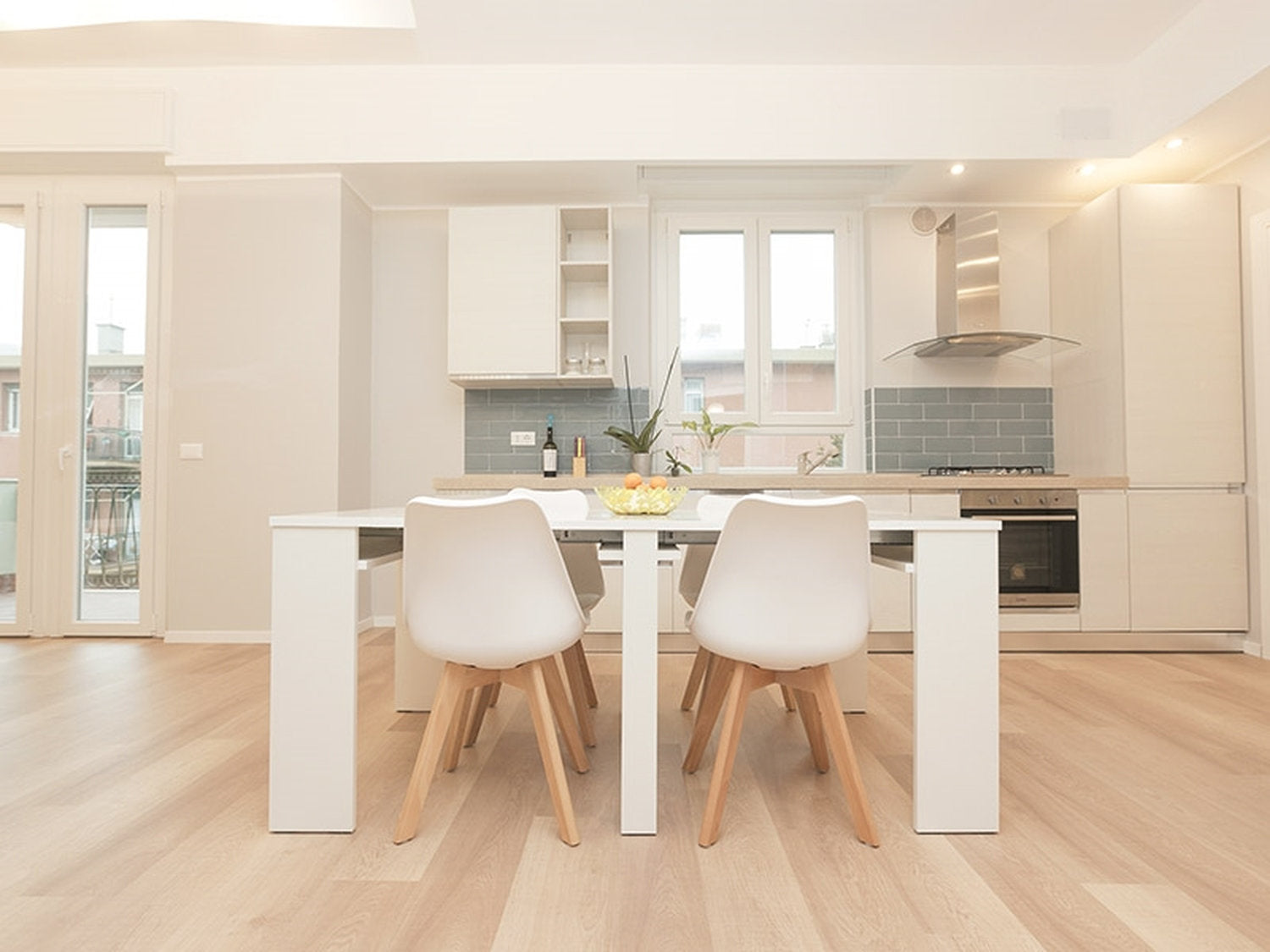 Cucina e zona pranzo con mobili bianchi e pavimento in laminato effetto rovere chiaro della collezione Facile+ di Skema