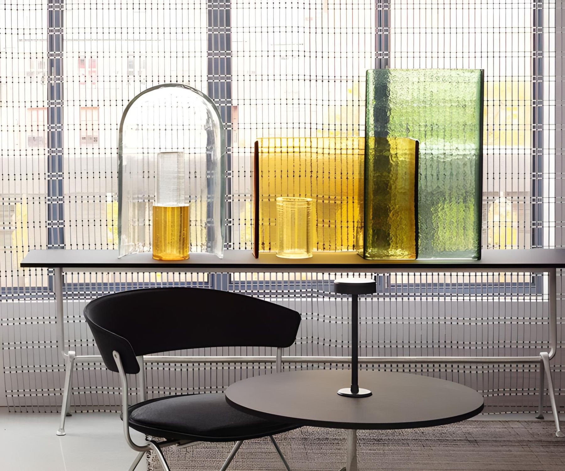 Zona lounge con tavolo rotondo, sedia imbottita nera e vasi decorativi in vetro colorato su fondo filtrante