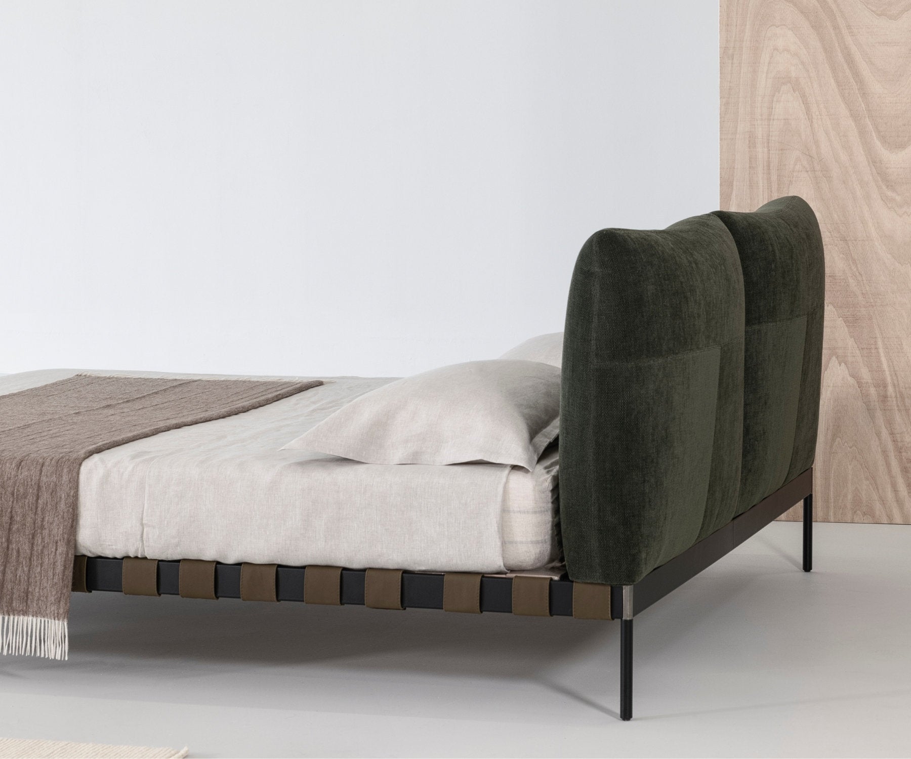 Letto matrimoniale con testiera imbottita in velluto verde scuro e struttura a cinghie in vista