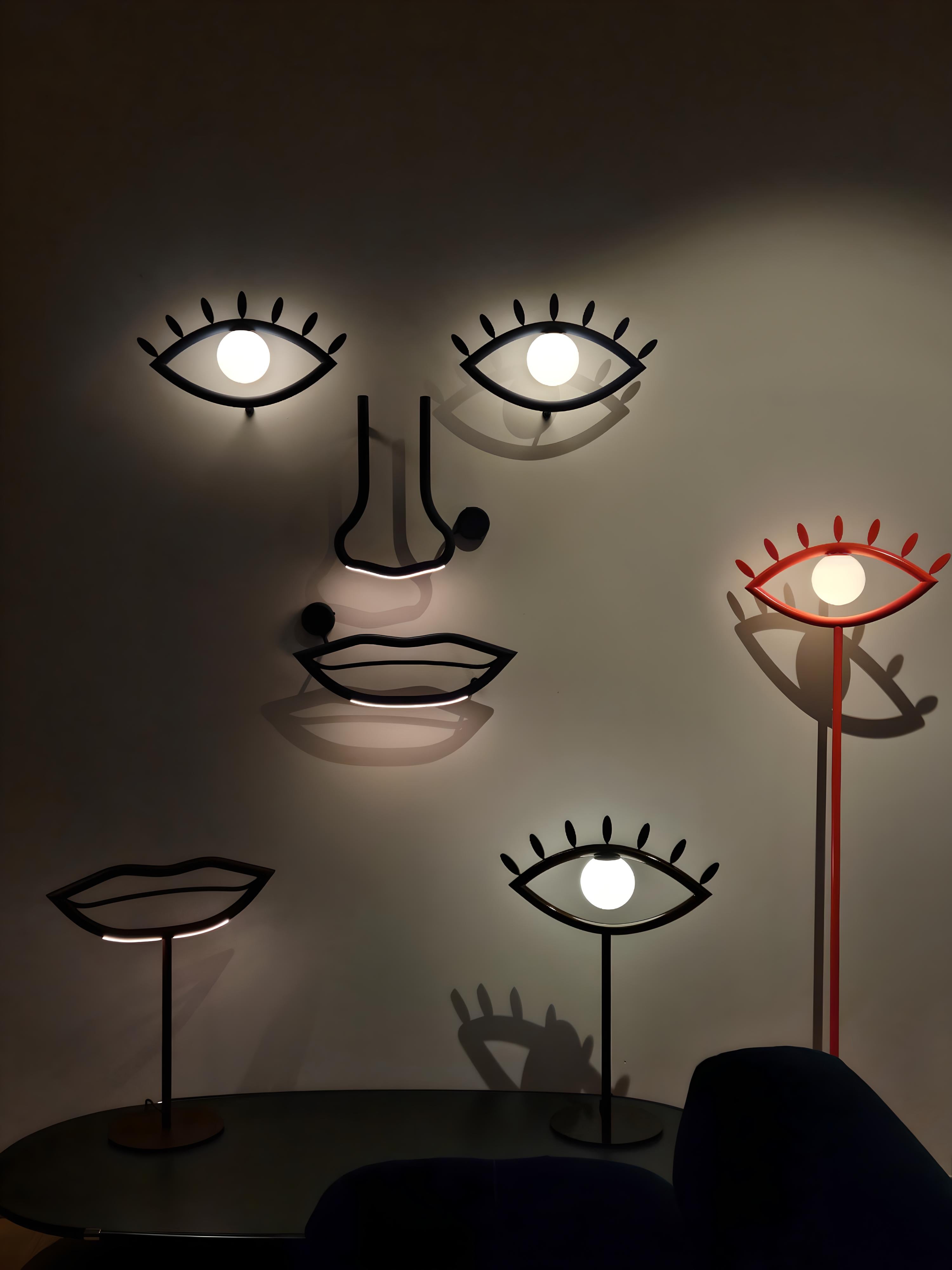 Lampade da tavolo Visio Masiero in versione occhio e bocca, accostate alla composizione luminosa a parete