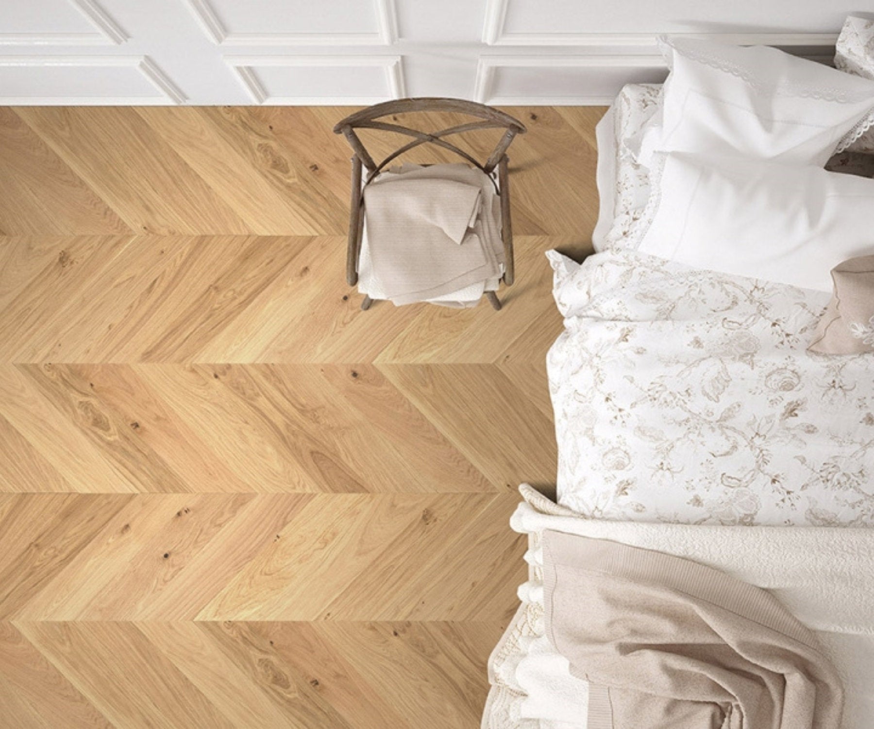 Vista dall’alto di una camera da letto con pavimento in legno chiaro posato a spina ungherese, accanto a letto con biancheria chiara e sedia in legno
