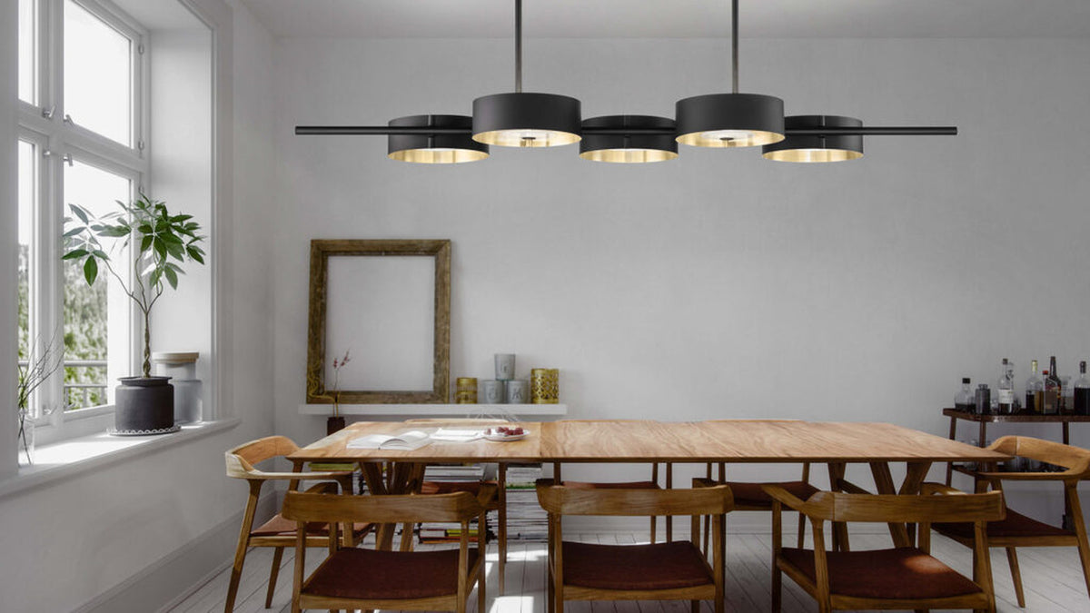 Sound BIL5 di Masiero, lampadario lineare a 5 luci in metallo nero e vetro, sospeso sopra un lungo tavolo in legno.