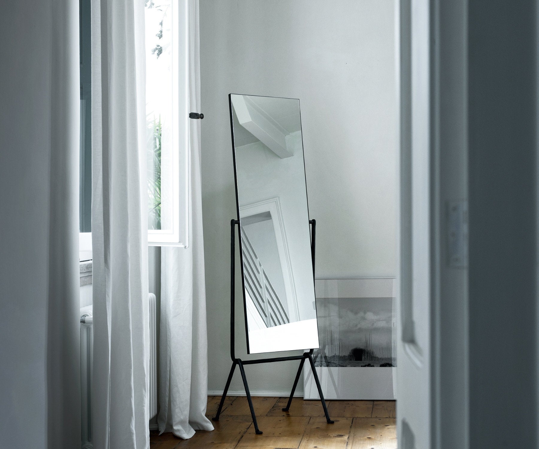 Specchio autoportante inclinato con struttura in metallo antracite in una stanza luminosa con pavimento in legno