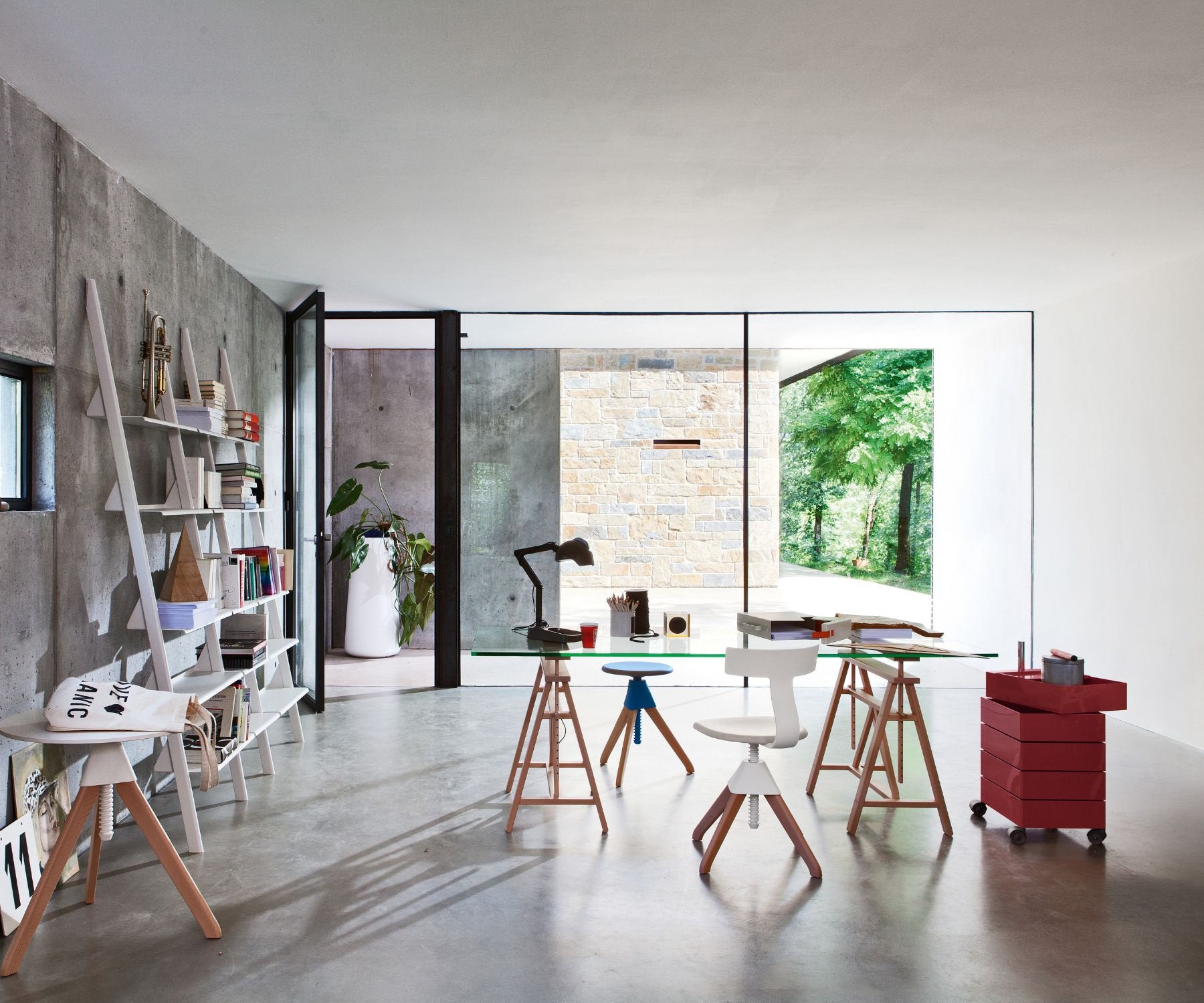 Spazio ufficio con tavoli in vetro, sedie ergonomiche, scaffalatura e luce naturale da pareti vetrate su fondo in cemento