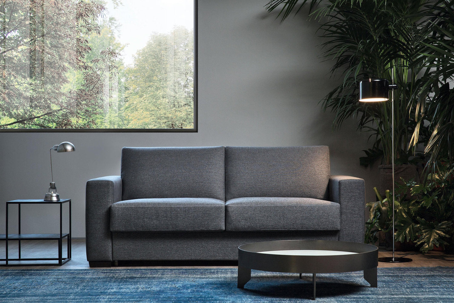 Divano letto Magnum grigio inserito in un soggiorno contemporaneo con ampie vetrate