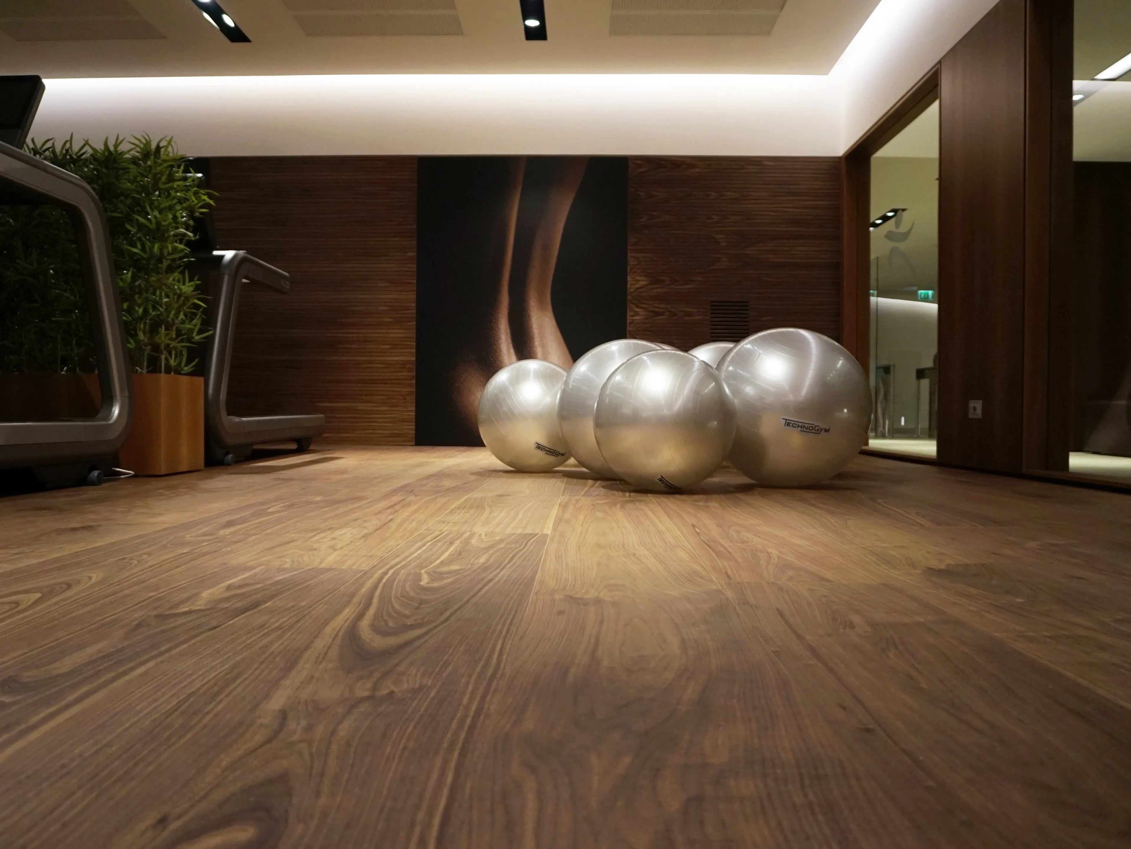 Sala fitness con parquet effetto noce e attrezzi ginnici, illuminazione soffusa e atmosfera calda