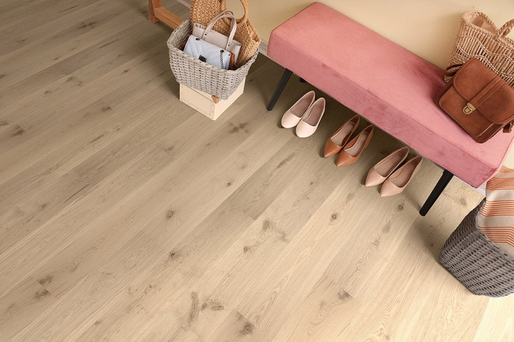 Ingresso con parquet chiaro in Rovere Trissino della linea Palladio Skema, finitura naturale e nodi visibili, panca in velluto e accessori in vimini.