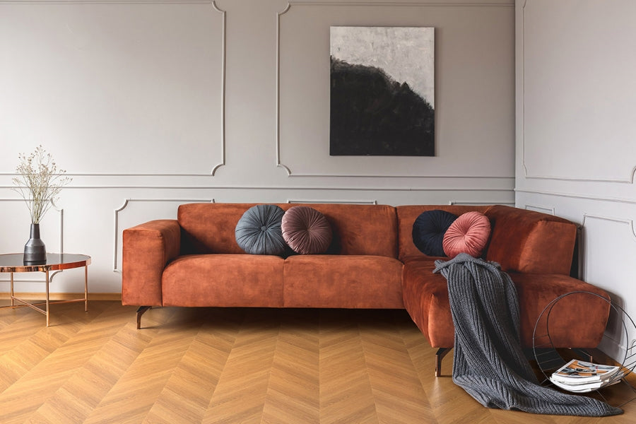 Salotto con divano angolare color ruggine e pavimento StarKs Skema in posa a spina francese su fondo effetto rovere