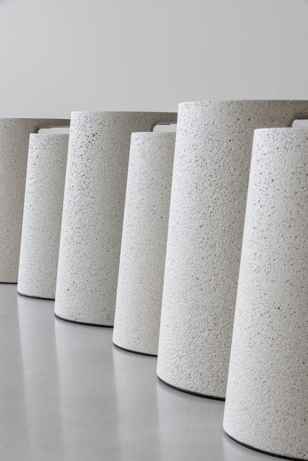 Serie di basi dei tavolini Ancora Magis in cemento a vista, allineate su pavimento grigio