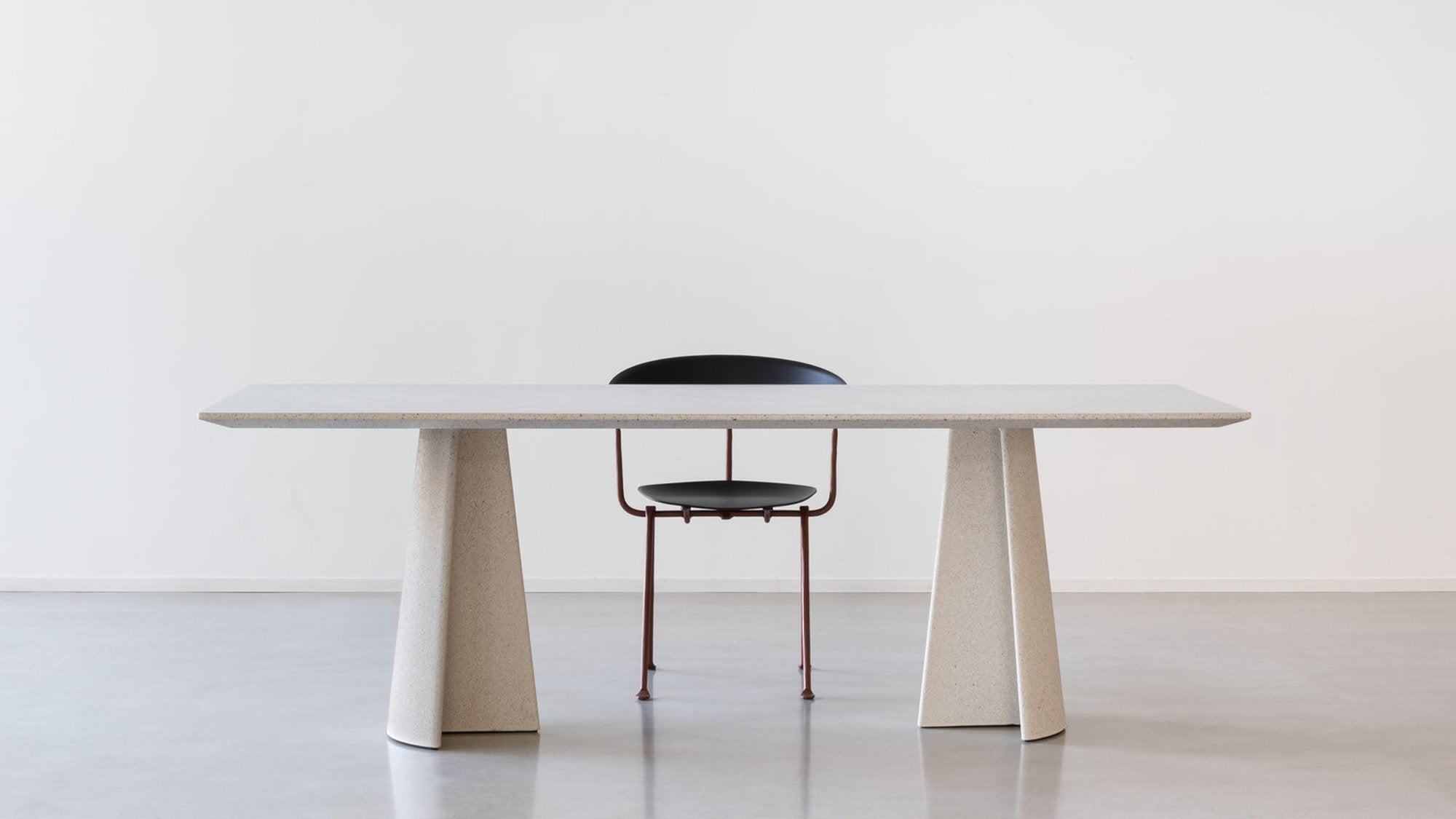 Primo piano del piano in cemento del tavolo Ancora Magis, con sedia nera sfocata sullo sfondo