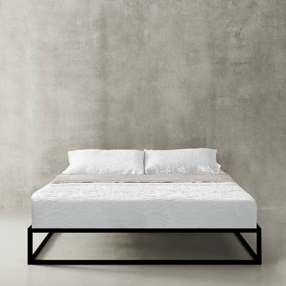 Letto Asha Basic con struttura nera opaca e biancheria chiara su sfondo grigio cemento