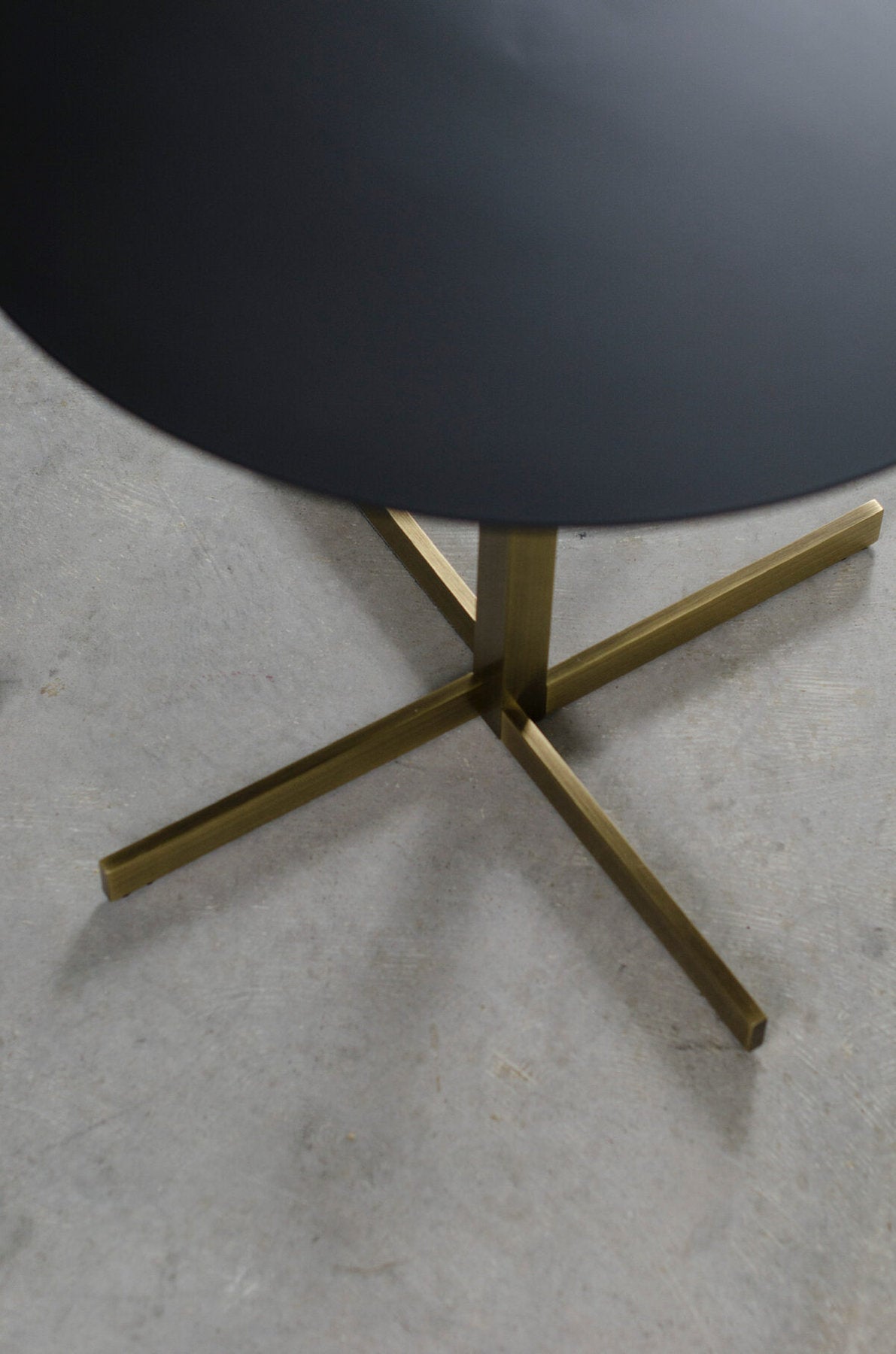 Dettaglio base incrociata in ottone satinato del tavolino Xo Brass  di xam su pavimento  cemento 