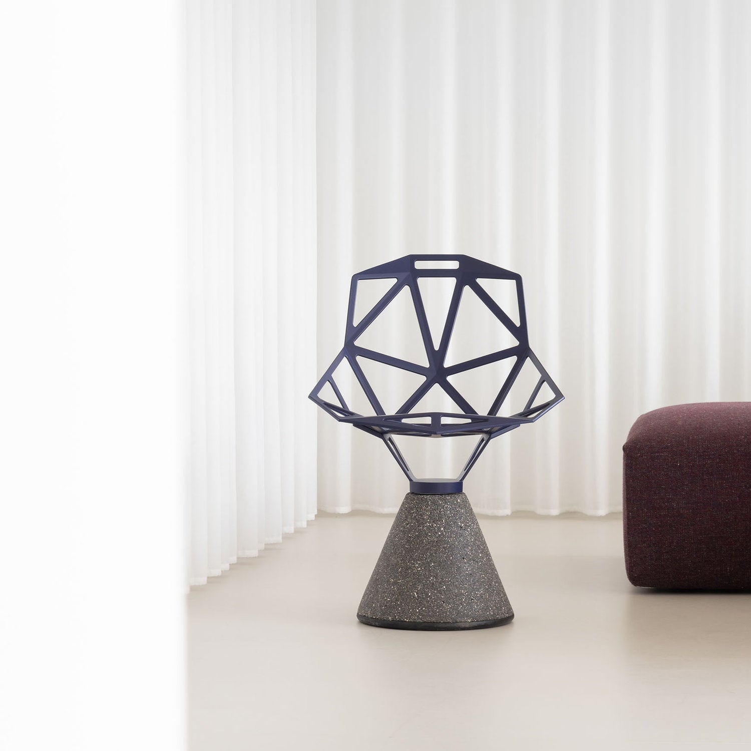 Sedia Chair One Concrete Magis con seduta blu viola e base in cemento, ambientata in un interno minimale con tende bianche e pouf bordeaux