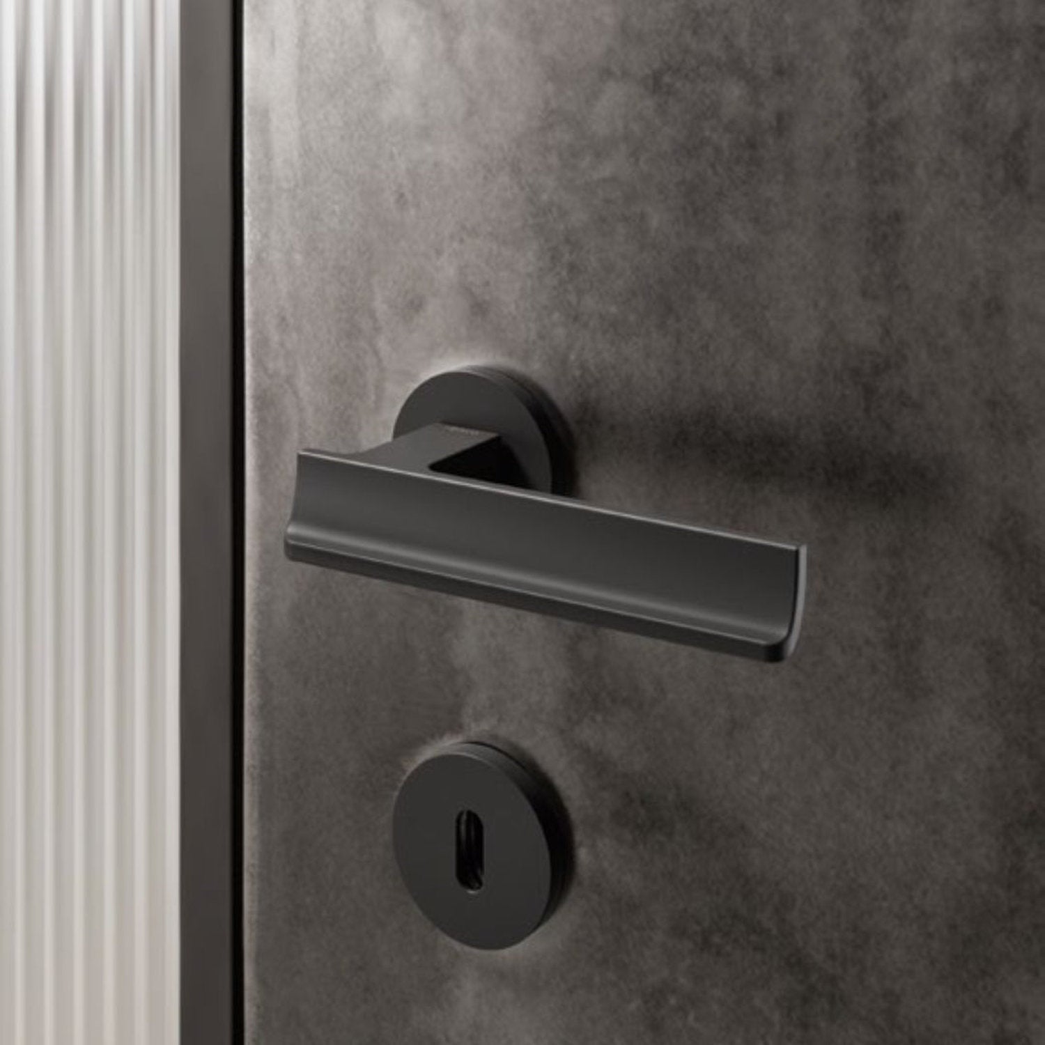 Maniglia nera opaca su porta in finitura materica scura, con rosetta tonda e design contemporaneo, installata in un ambiente living