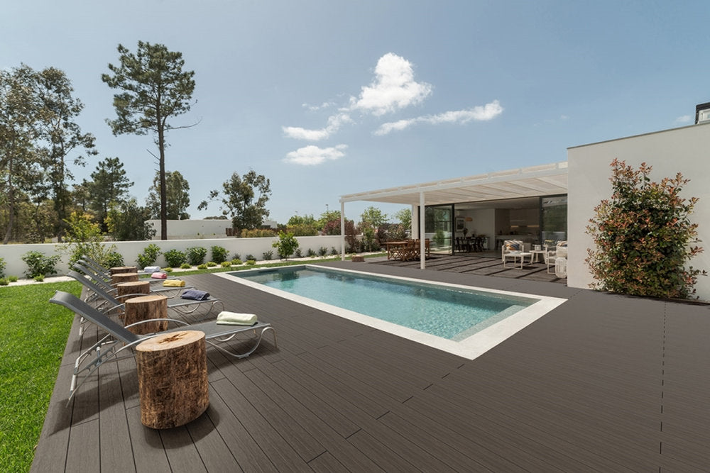 Rivestimento WPC Marina Pacto Skema in tonalità scura accanto a piscina e abitazione moderna