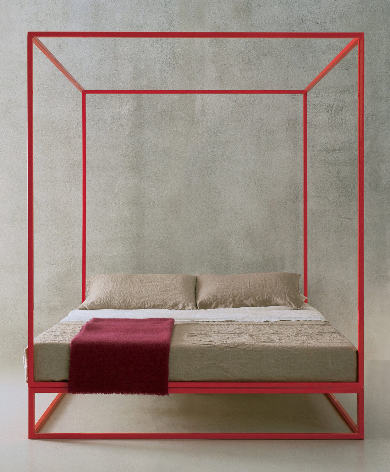 Letto a baldacchino Xam Asha in metallo rosso, parete cemento e biancheria beige con plaid bordeaux