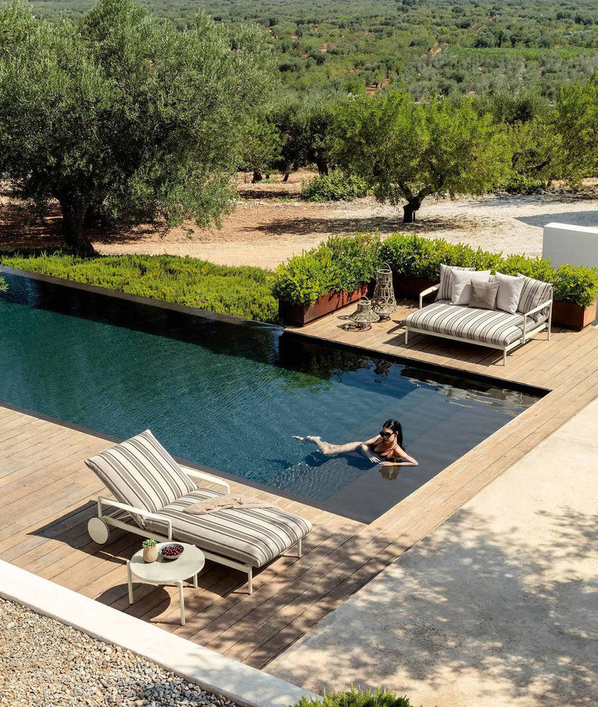 lettino outdoor Nalu di Talenti accanto alla piscina con rivestimento rigato e cuscini decorativi 
