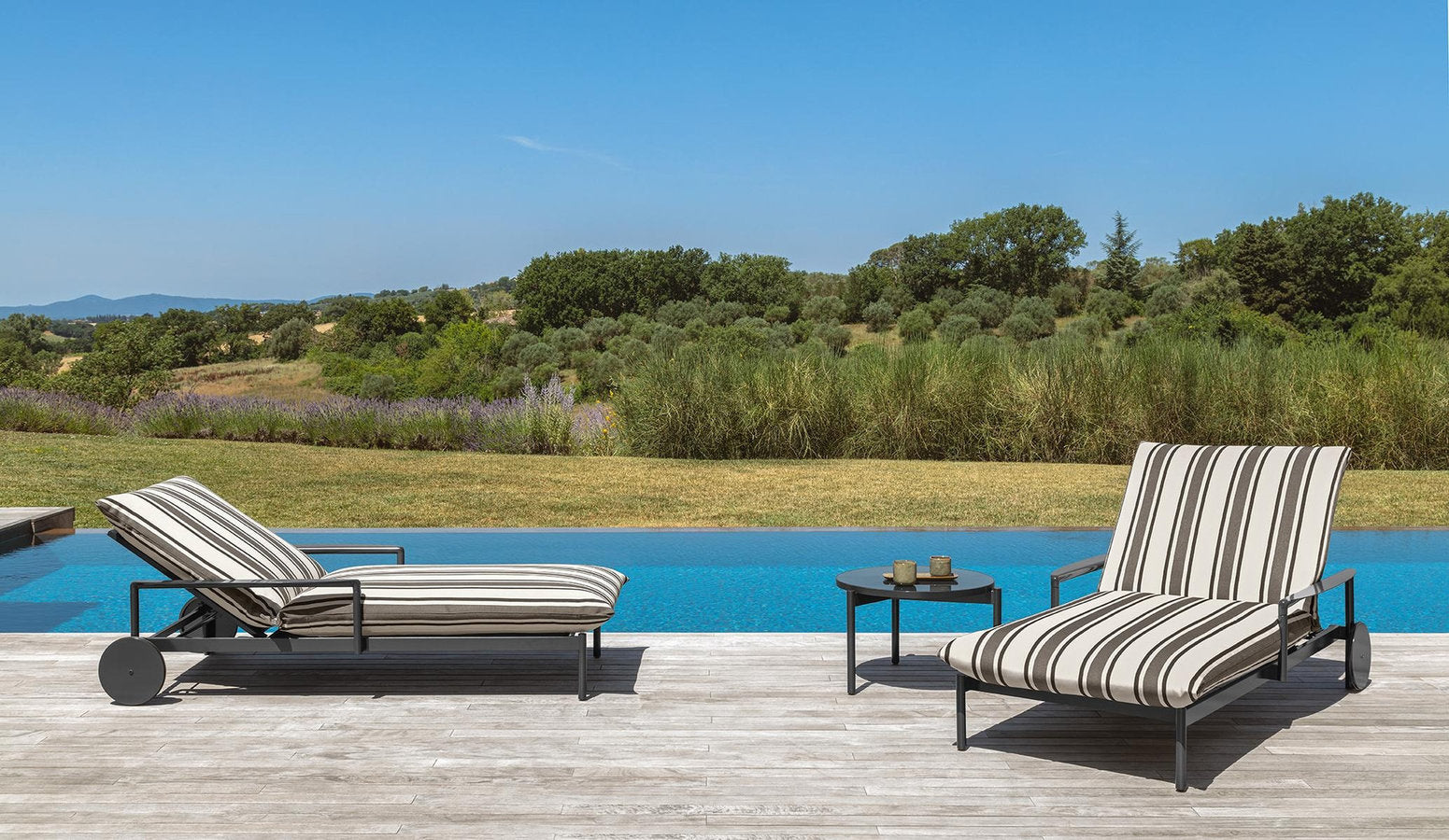 Due lettini piscina Nalu di Talenti con tavolino tondo su deck esterno a bordo vasca 