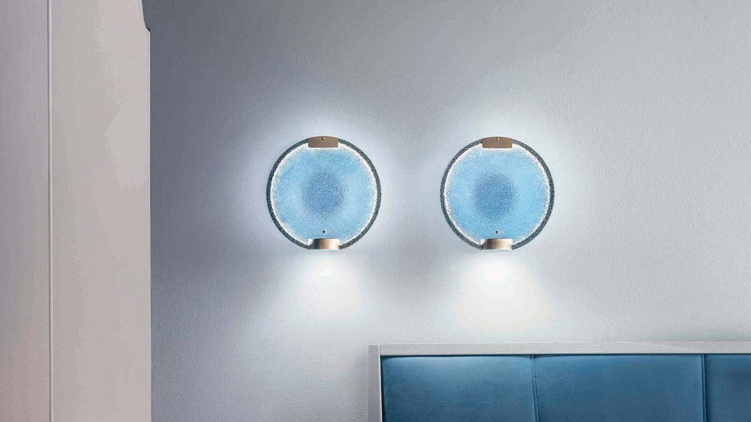 Due lampade da parete Horo by Masiero in vetro prismatico azzurro su parete grigia