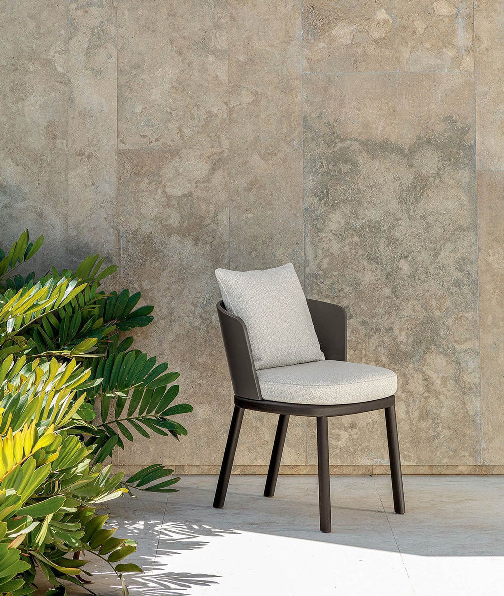 Sedia pranzo outdoor Itaca Talenti con struttura scura e cuscini chiari, su terrazza con parete materica