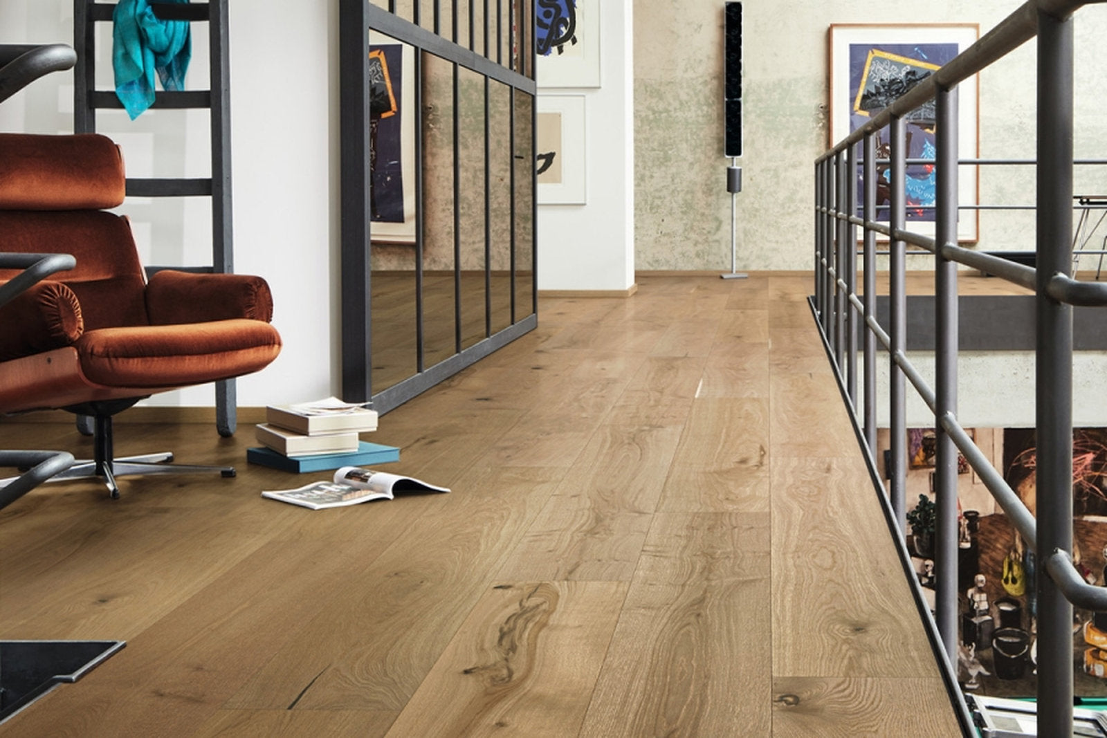 Ambiente loft con pavimento in legno scuro, poltrona in velluto color ruggine e balaustra in metallo