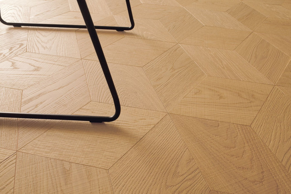 Pavimento Yles Hexagon in rovere Neutra con disegno geometrico e dettaglio di sedia in metallo.