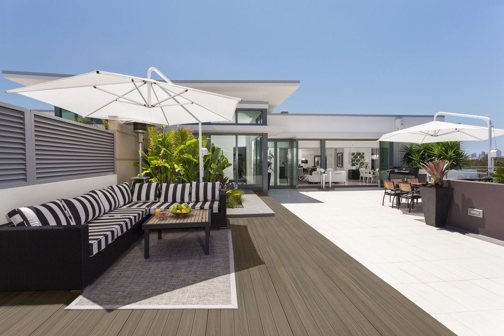 Pavimento WPC effetto legno su terrazza attico con divani da esterno e ombrelloni bianchi