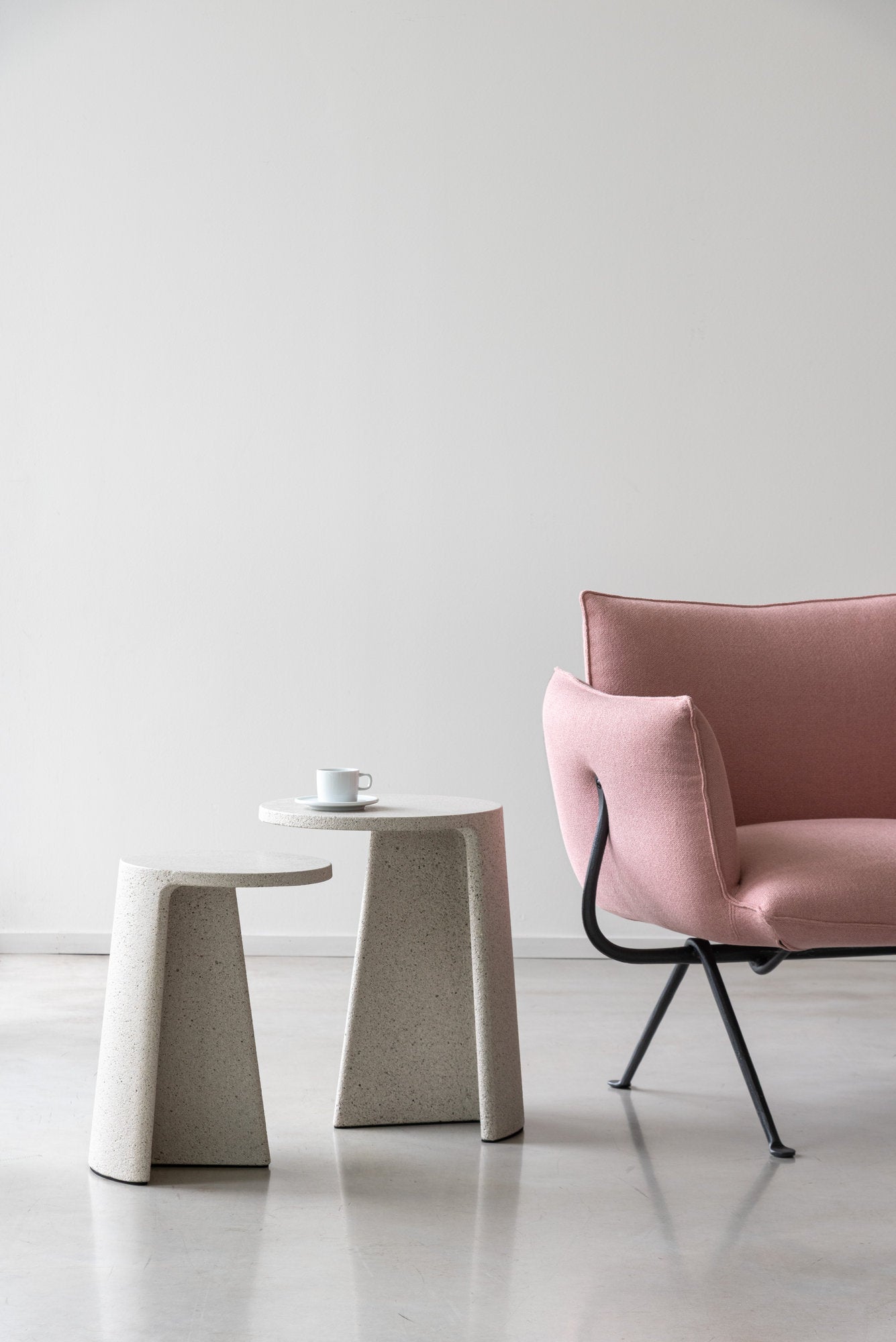 Due tavolini Ancora Magis in cemento accanto a poltrona rosa, con tazza su piattino