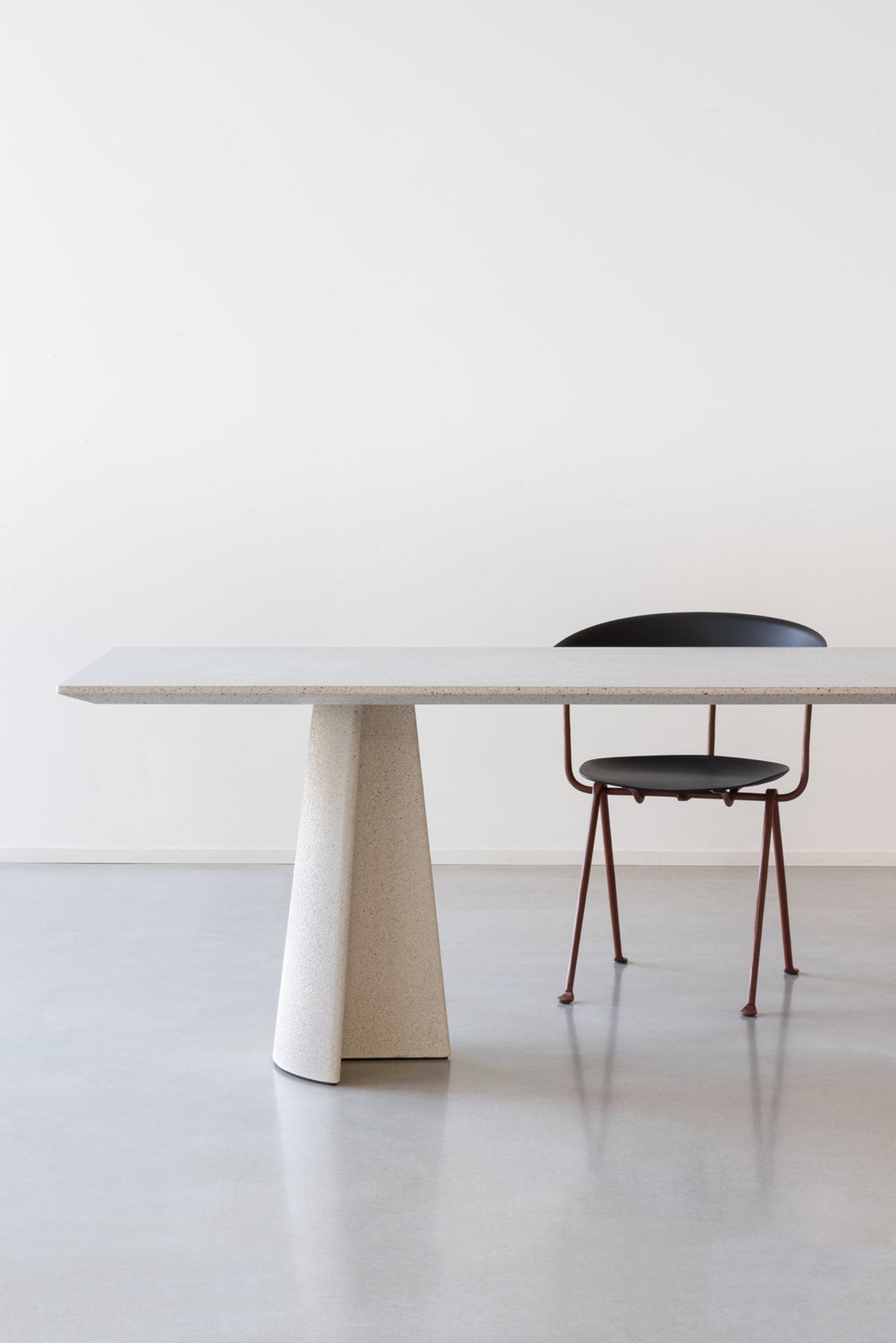 Vista laterale del tavolo Ancora Magis con piano in cemento e gamba in cemento, sedia nera dietro