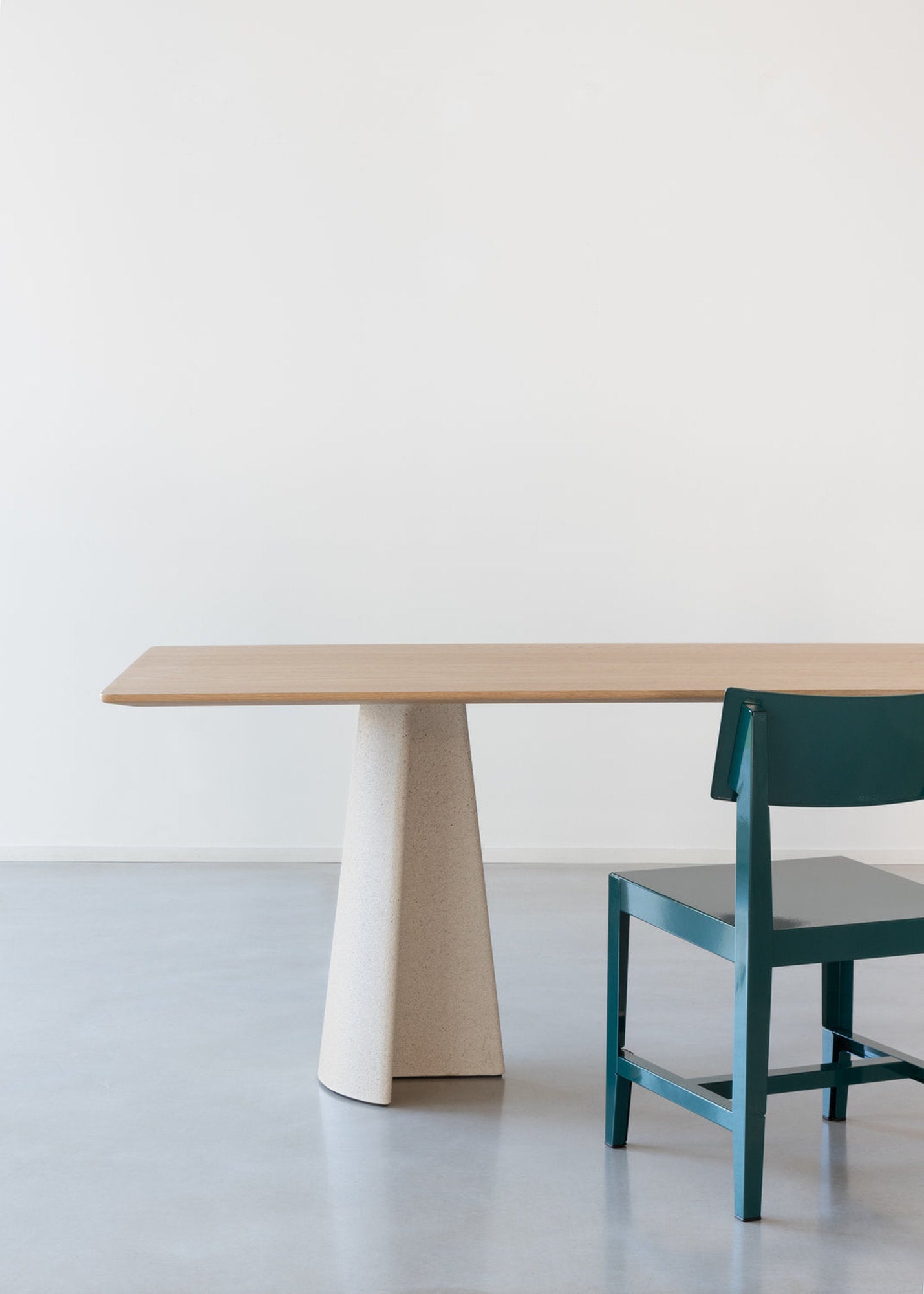 Dettaglio laterale del tavolo Ancora Magis con piano in rovere e gamba in cemento, sedia verde a destra