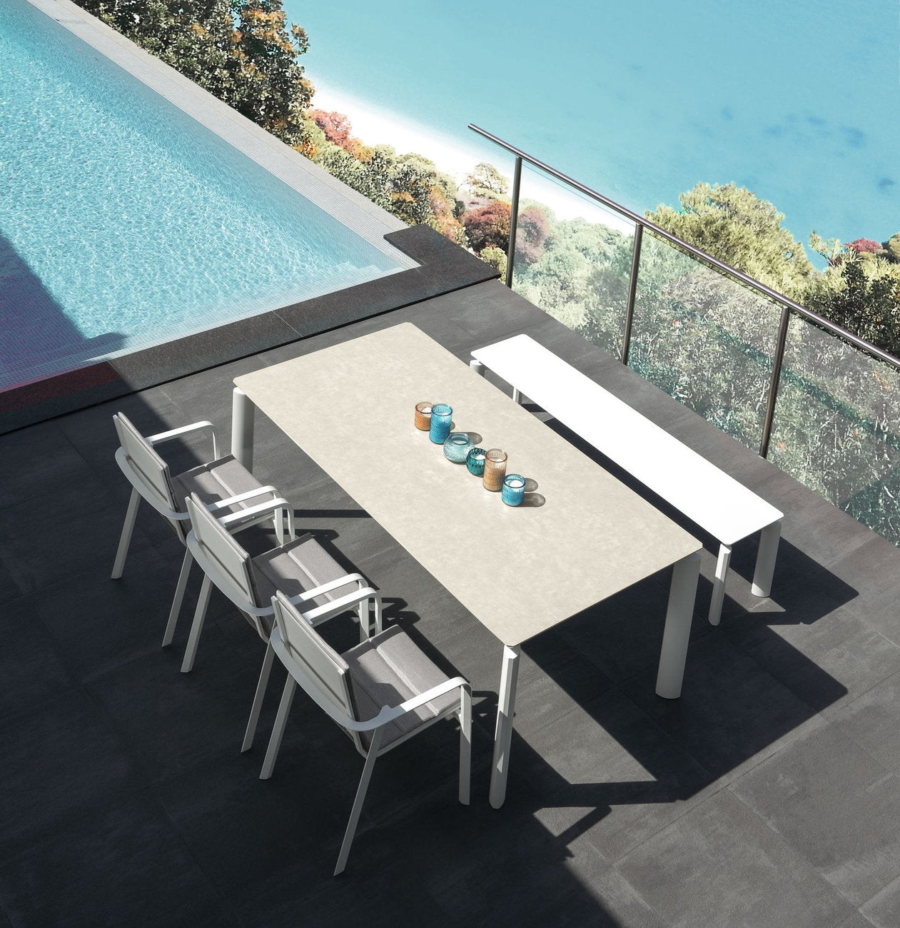 Tavolo da esterno Milo Talenti con piano in ceramica chiara, sedie e panca a bordo piscina