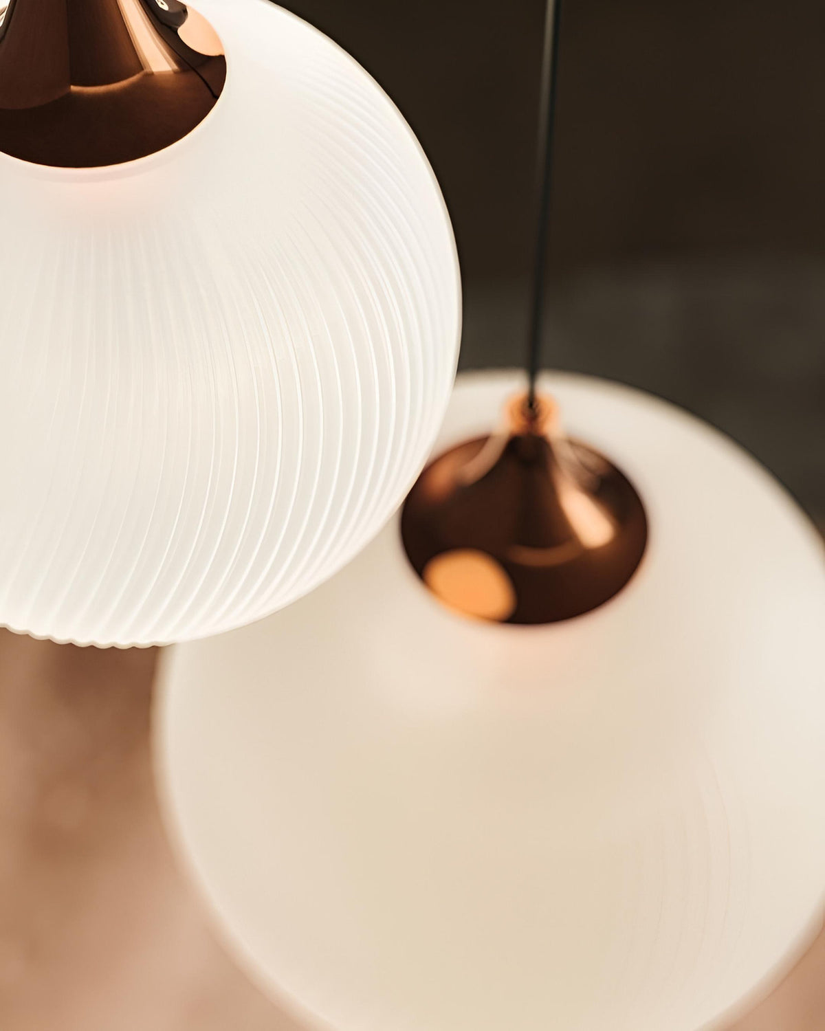 Dettaglio delle lampade a sospensione Tee di Masiero, con diffusori sferici in vetro bianco rigato e supporti metallici ramati.